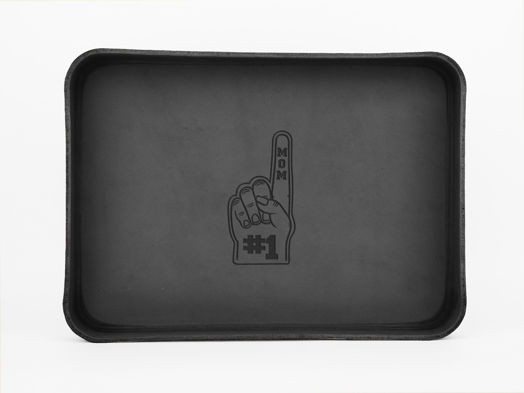 A black rectangular tray with a line drawing of a foam finger in the center. The finger points up and reads MOM on the finger and #1 on the palm, symbolizing Number 1 Mom.