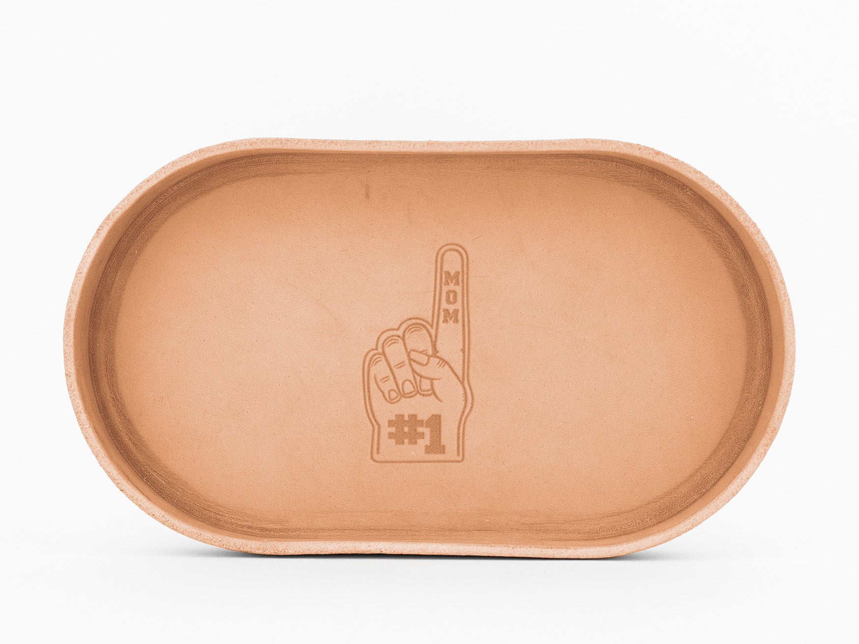Oval-shaped, natural colored leather tray with an engraved design of a hand holding up one finger. The finger has MOM written vertically, and below the hand, it says #1.