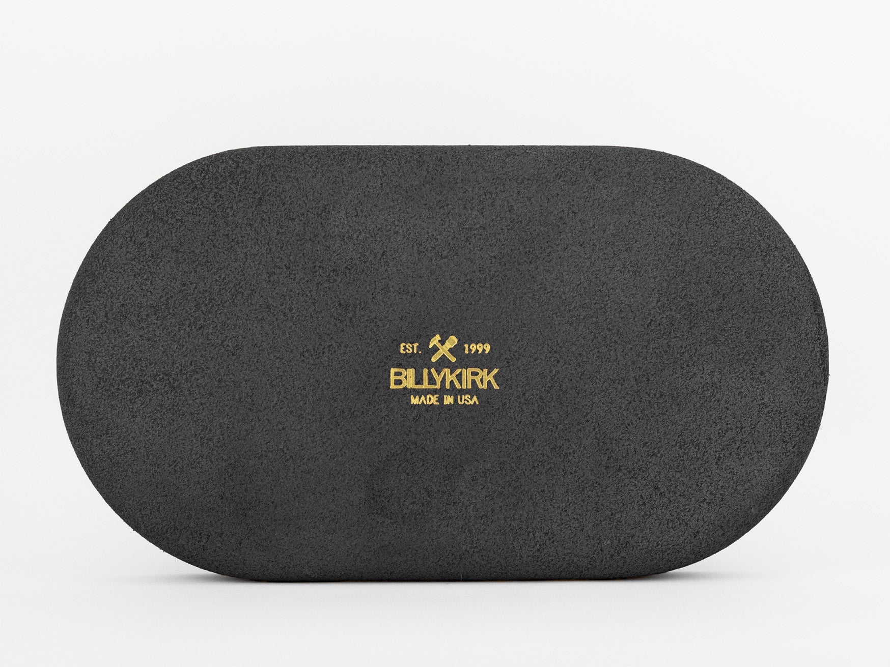 An oval-shaped black textured object with the words EST. 1999 BILLYKIRK MADE IN USA and a hammer and pickaxe logo printed in gold at the center against a white background.