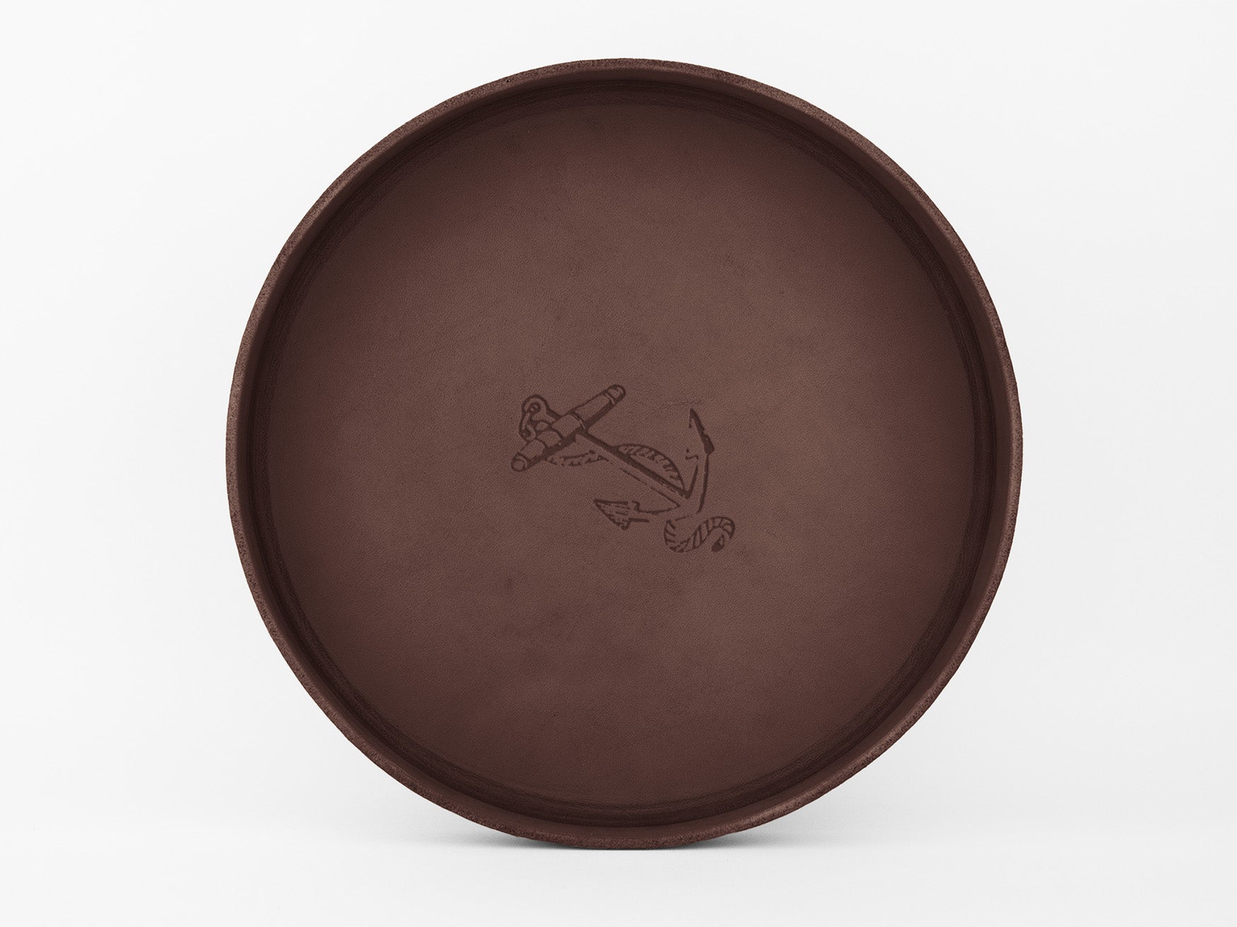 	
A round, brown leather tray with a simple anchor and rope design engraved in the center, set against a plain white background.