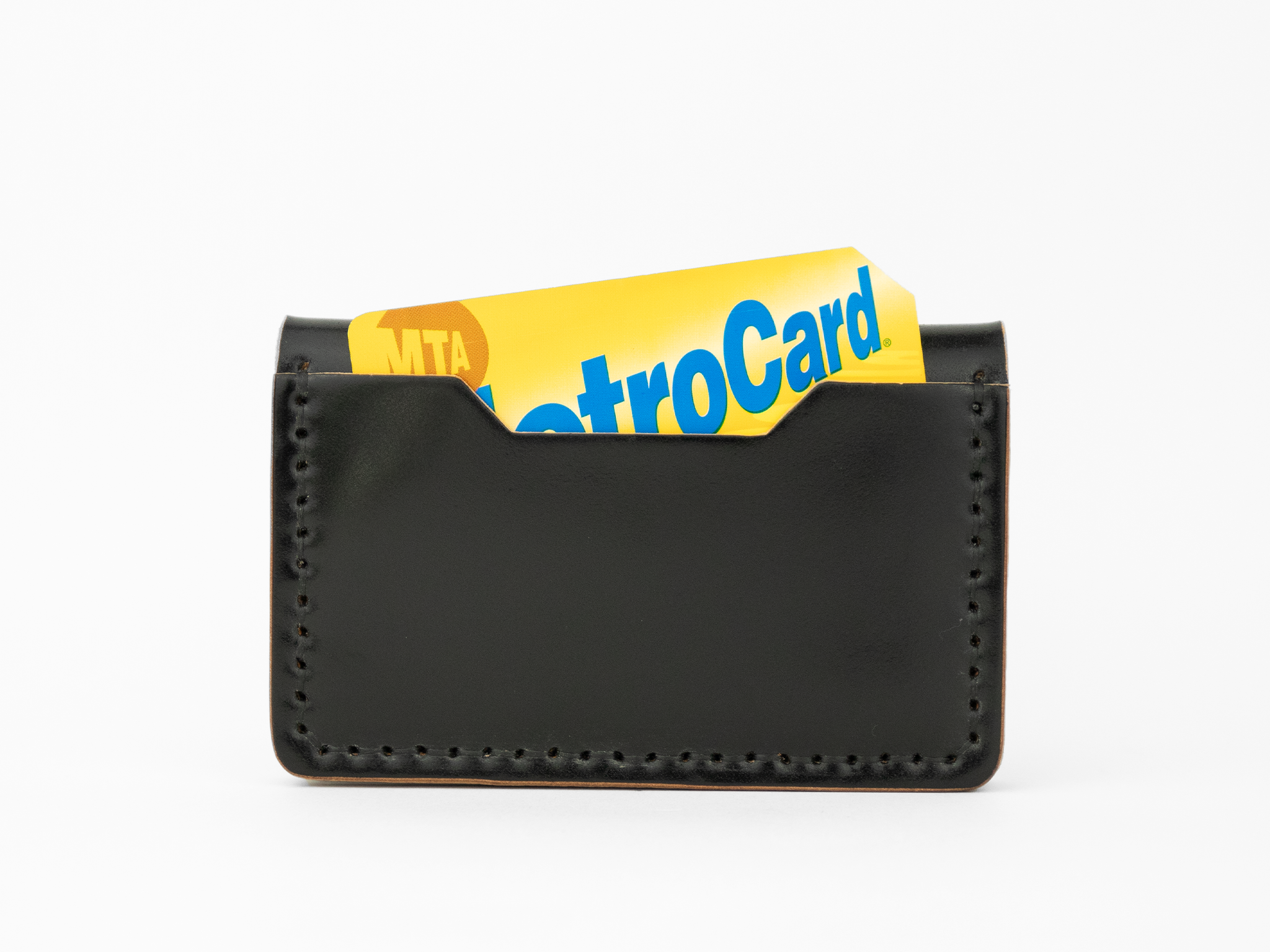 A black cordovan leather card holder with visible stitching holds a yellow and blue MTA MetroCard, partially sticking out from the top.