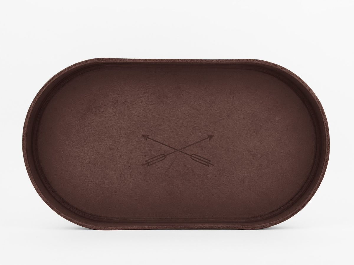 A brown oval tray with a minimalist design, featuring two crossed arrows engraved in the center, set against a plain white background.