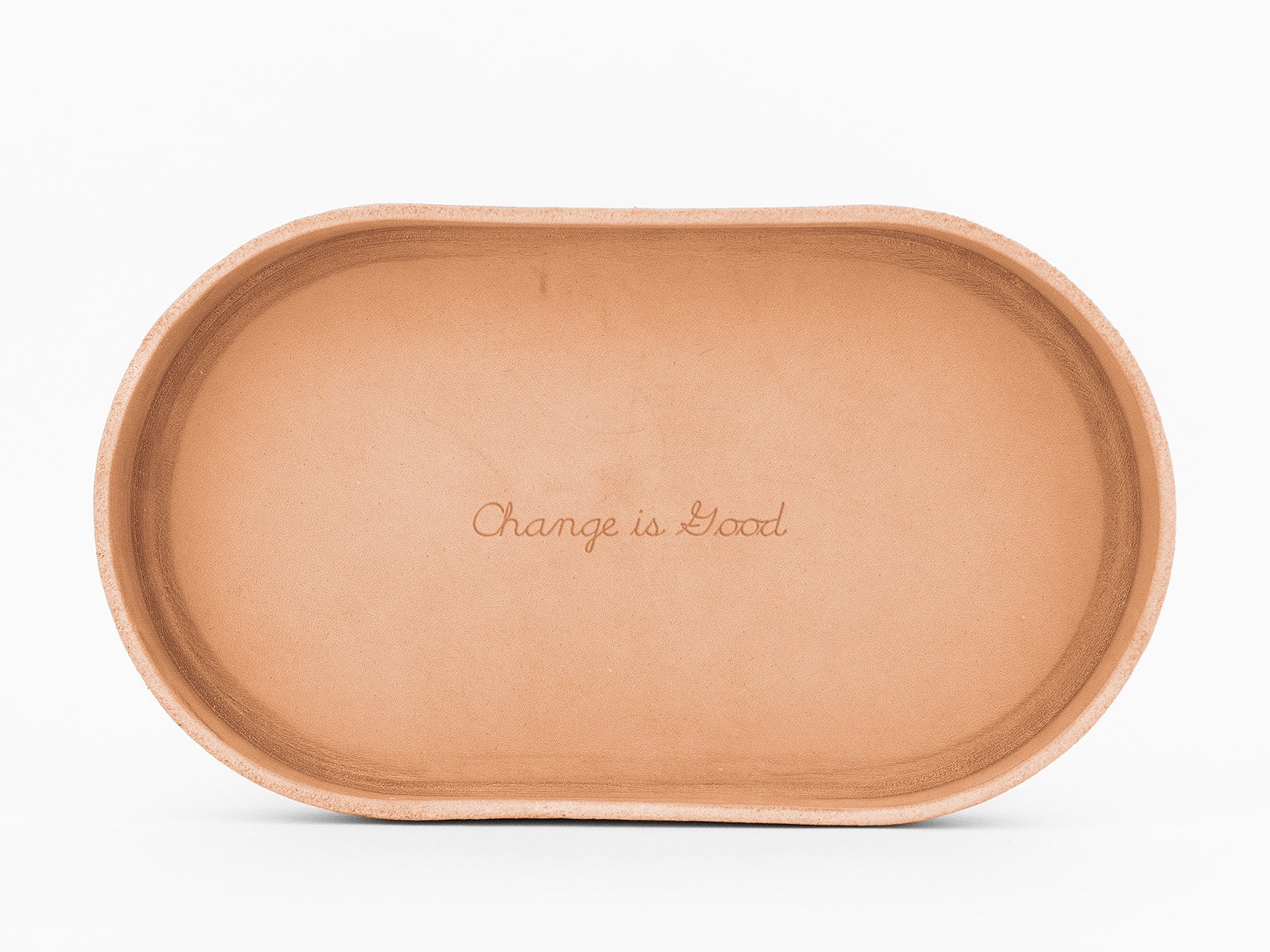 An oval-shaped, natural colored  tray the words Change is Good engraved in the center, photographed against a white background.
