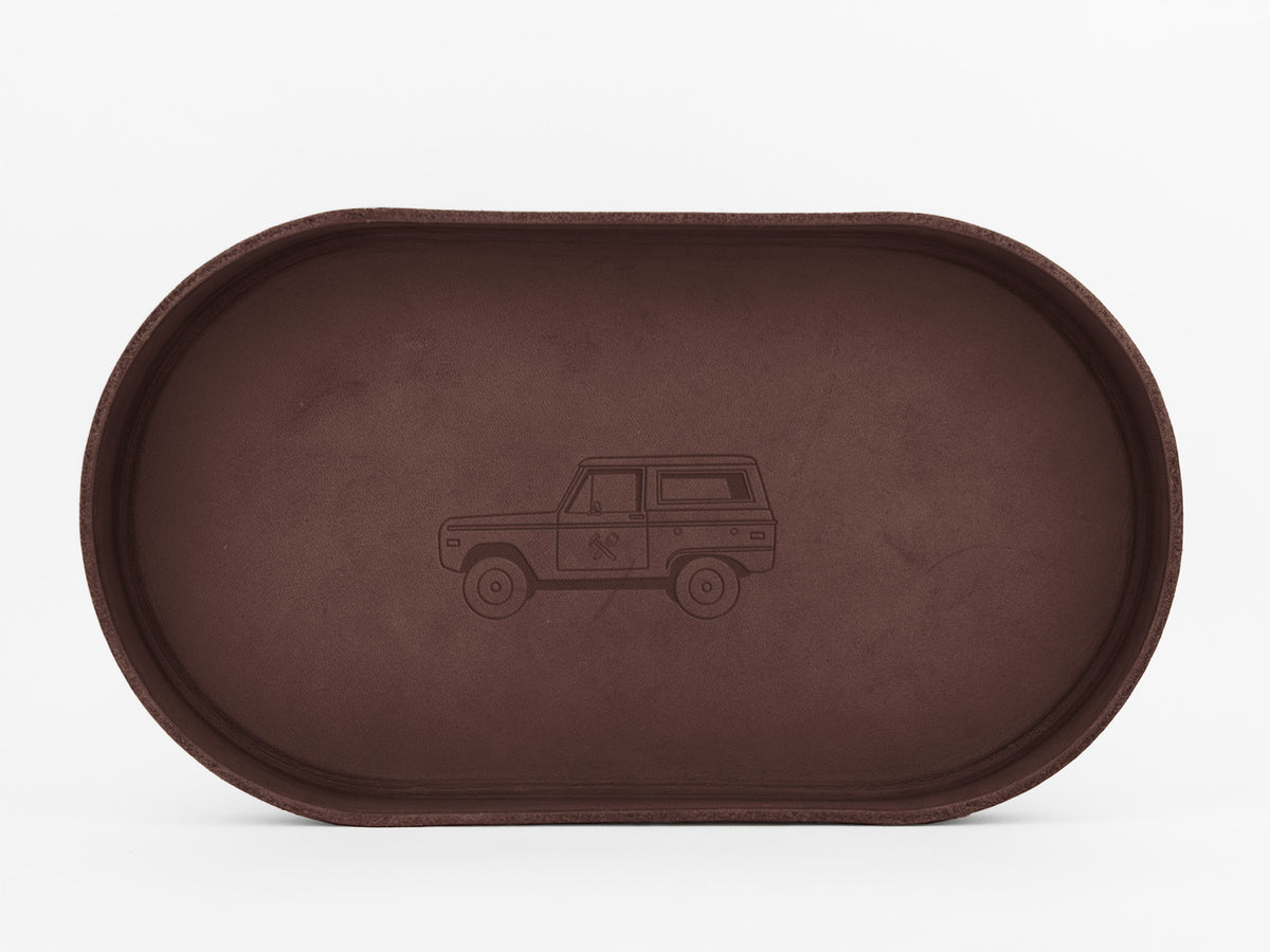A brown oval tray with an engraved outline of a classic SUV-style car in the center, displayed against a white background.

