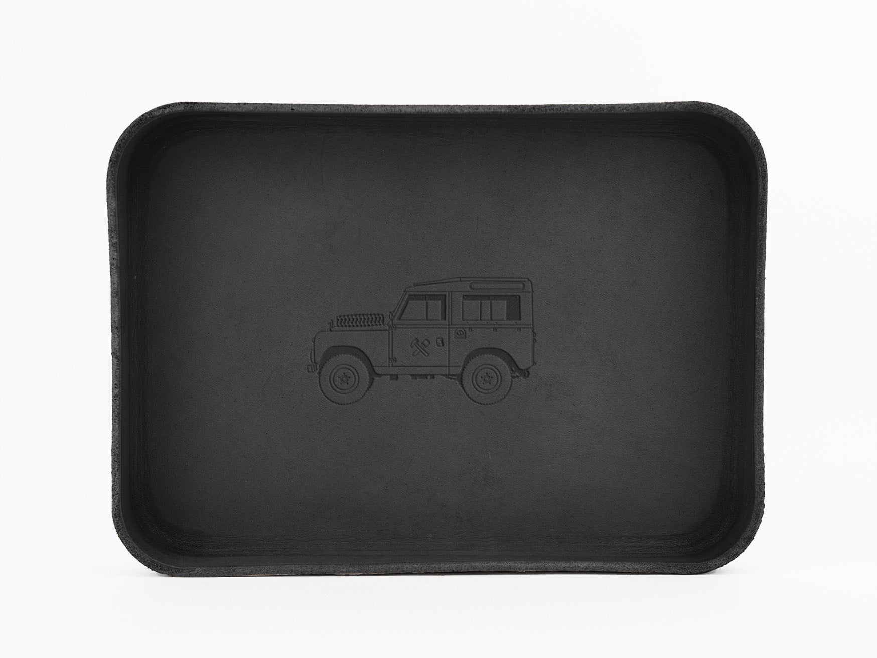 A black rectangular tray with rounded corners features a subtle engraved outline of a classic off-road vehicle, similar to a Land Rover, centered inside the tray. The background is plain white.