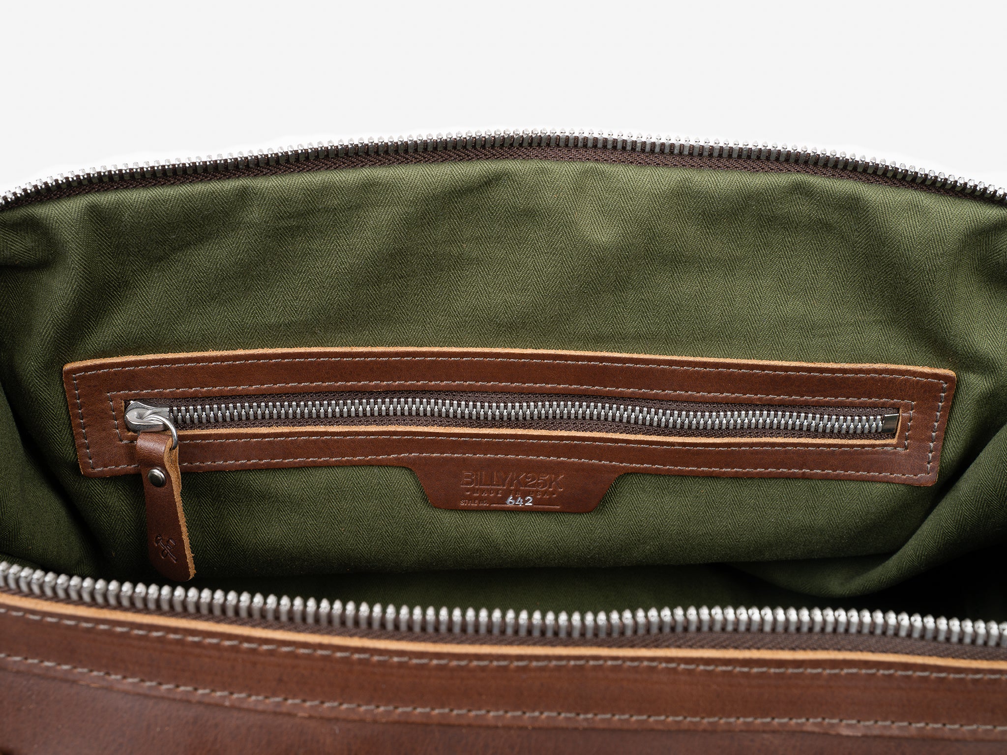 A close-up view of the inside of a brown leather bag, showing a green fabric lining and a zippered inner pocket with leather trim and a metal zipper pull. The brand name Billykirk is embossed on the leather.