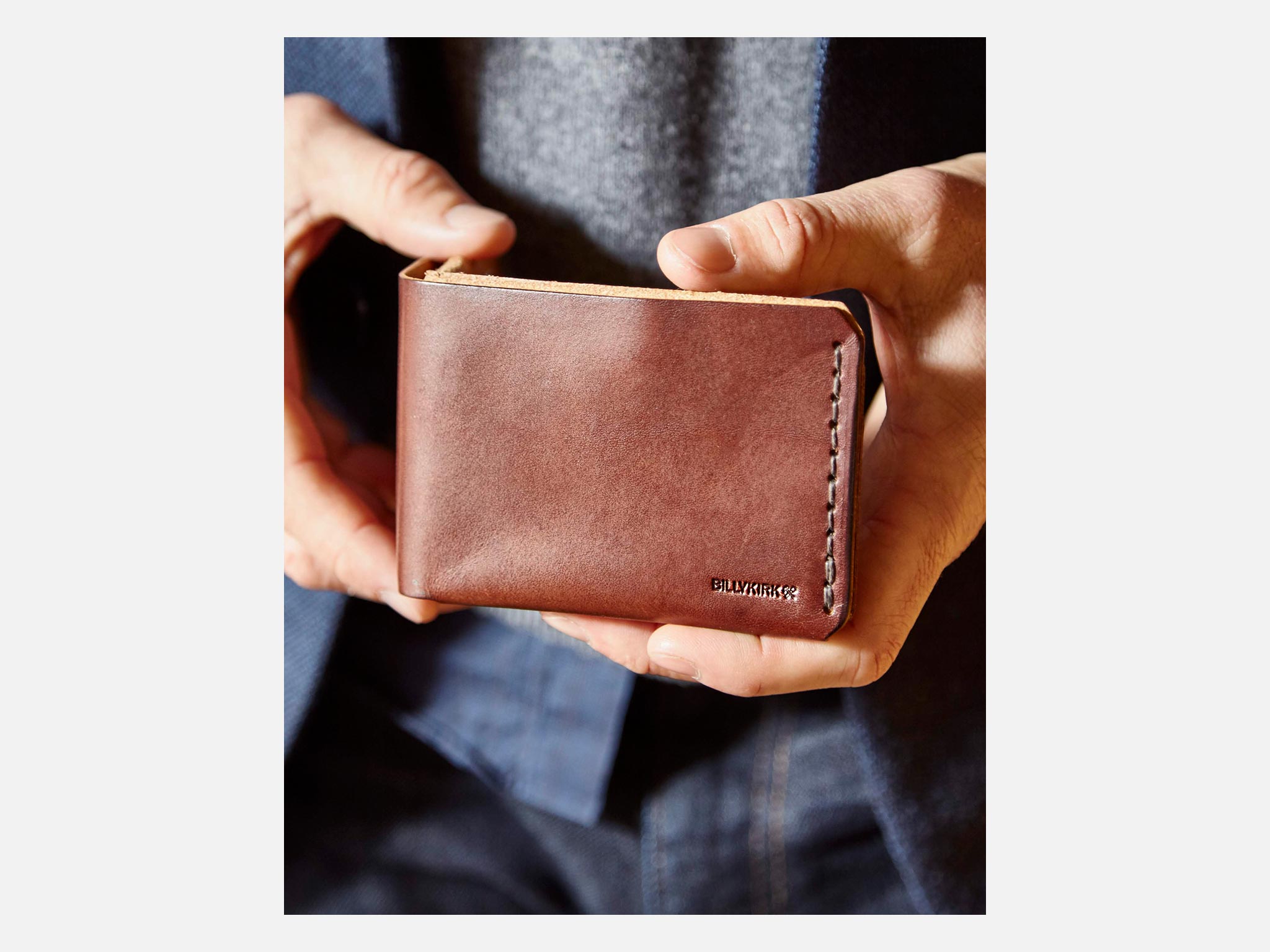 A black leather wallet is open, displaying a $20 bill and several credit and ID cards neatly organized in its slots against a white background.