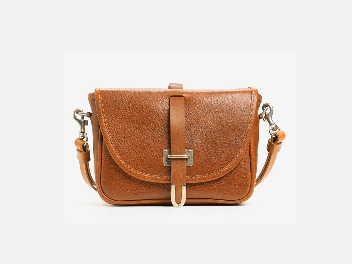 A small brown leather crossbody bag with a curved flap, metal buckle closure, and adjustable strap, displayed on a plain white background.