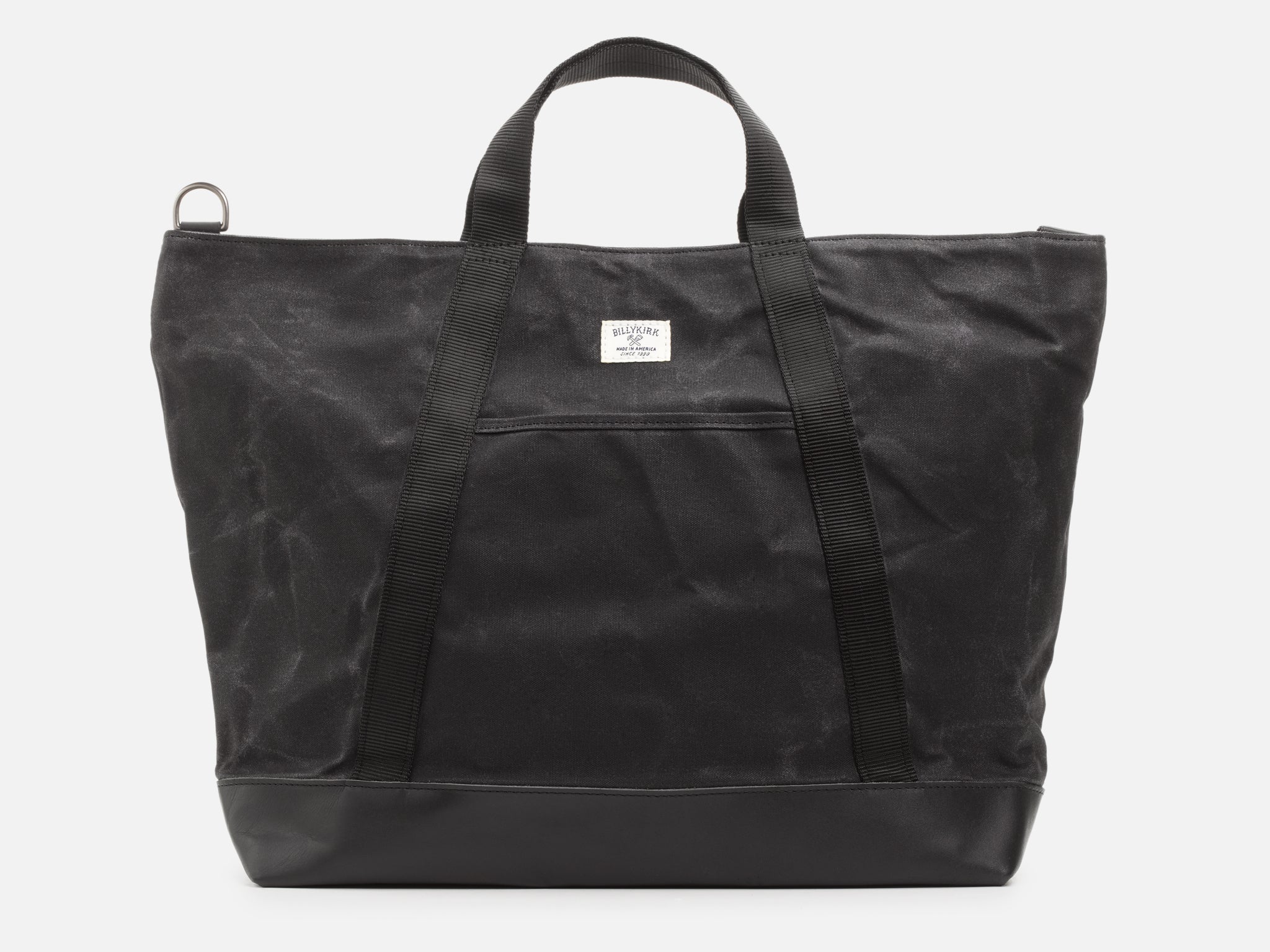 A back view of an black waxed canvas tote bag with 1" nylon black handles with pocket between the handles, and a black leather bottom, set against a plain white background.