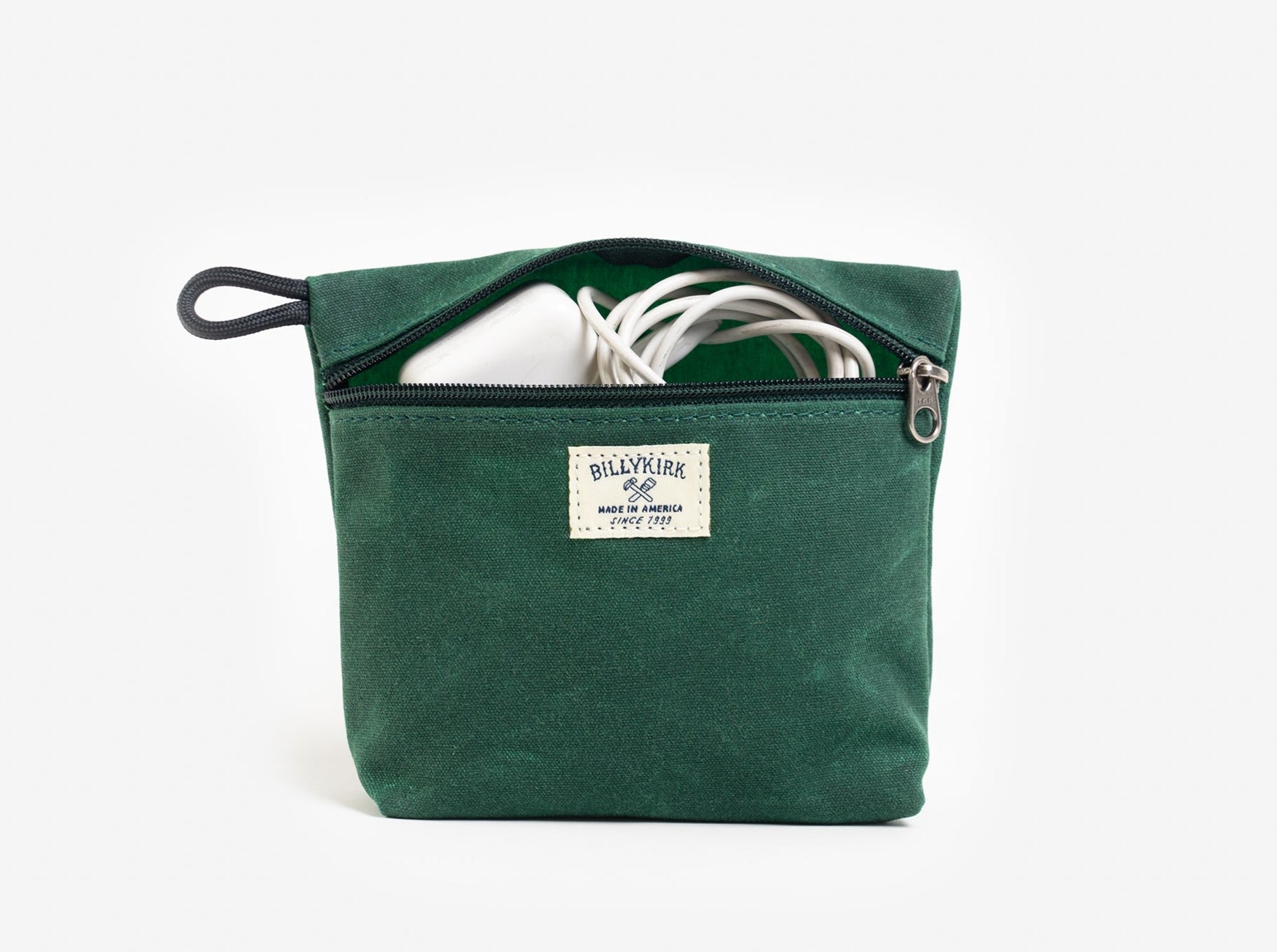 A green waxed canvas pouch with zipper closure on a neutral background. It features a cream woven tag that reads "Billykirk made in america since 1999" and has a white cord coming from the pouches opening.